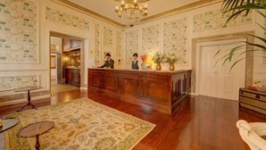 Un vestíbulo con mostrador de recepción, piso de madera, papel tapiz estampado y un candelabro.