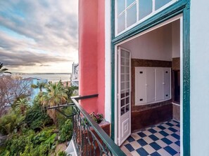 A balcony with a checkered floor, a view of the sea, and a door leading to a room with a tiled wall and a cabinet. - Palácio das Especiarias (Lisbon)