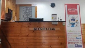A reception desk with a sign reading "INFORMATION" and a welcome sign for "KIM'S STAY9 GUEST HOUSE" with multilingual greetings. - Kimstay9 (Seoul)