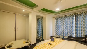 Habitación de hotel con cama, zona de estar curva, armario y ventana con cortinas estampadas.