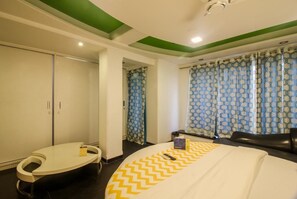 A hotel room with a bed, a curved seating area, a wardrobe, and a window with patterned curtains. - Fabhotel Panchvati Residency Andheri West (Mumbai)