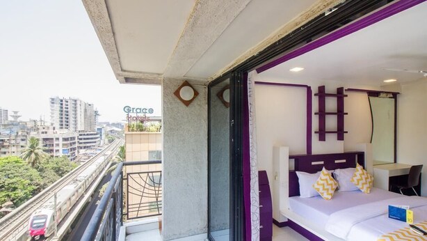 Habitació d'hotel amb un balcó, un llit amb roba de llit blanca i almoades grogues, una taula de treball i vista a la ciutat.