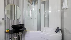 Un baño moderno con ducha de mampara de vidrio, un espejo redondo, un lavamanos negro y una bañera blanca.