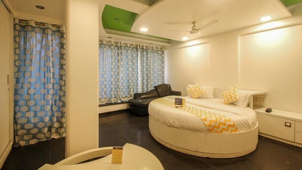 Quarto moderno com cama curva, ventilador de teto e janela com cortinas estampadas.