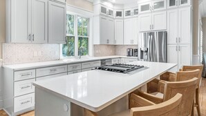 Eine moderne Küche mit weißen Schränken, einer großen Kochinsel mit Gaskochfeld und einem Kühlschrank.