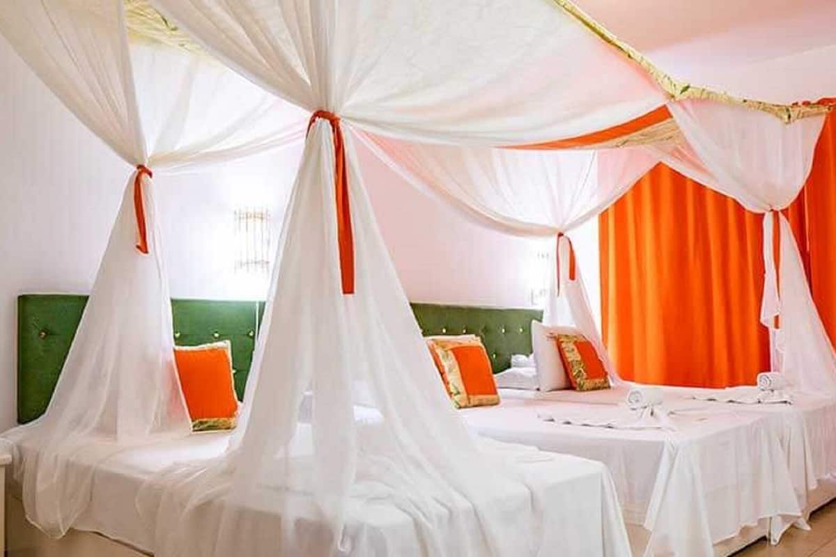 Ein Hotelzimmer mit zwei Betten, jeweils mit Baldachin, Nachttisch und grünem Kopfteil.