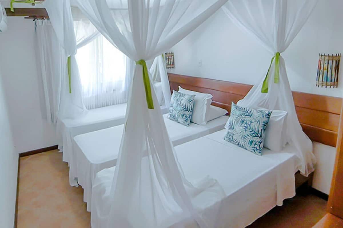 Ein Hotelzimmer mit zwei Betten, jeweils mit Baldachin, weißer Bettwäsche und einem hölzernen Kopfteil.