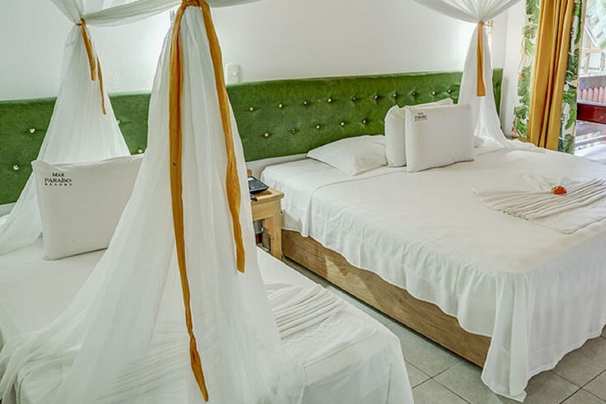 A four-poster bed with white linens and a green upholstered headboard.