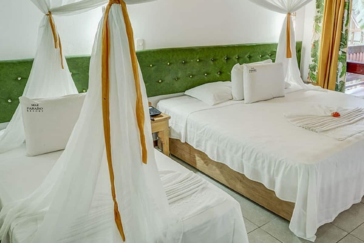 Ein Himmelbett mit weißen Bettwäsche und einem grünen, mit Stoff bezogenen Kopfteil.