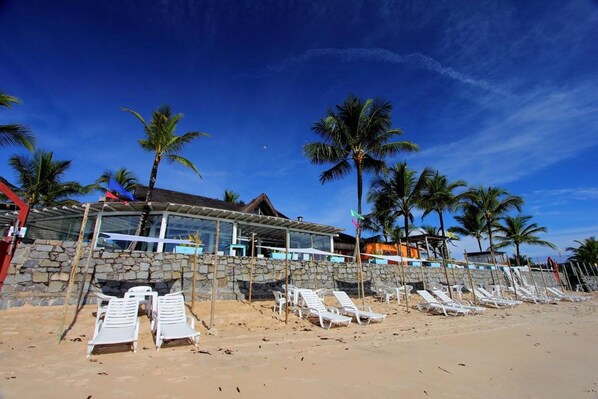 A beachside hotel with a stone facade, white lounge chairs, and palm trees. - Mar Paraiso Hotel (Porto Seguro)