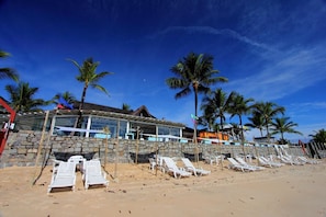 A beachside hotel with a stone facade, white lounge chairs, and palm trees. - Mar Paraiso Hotel (Porto Seguro)