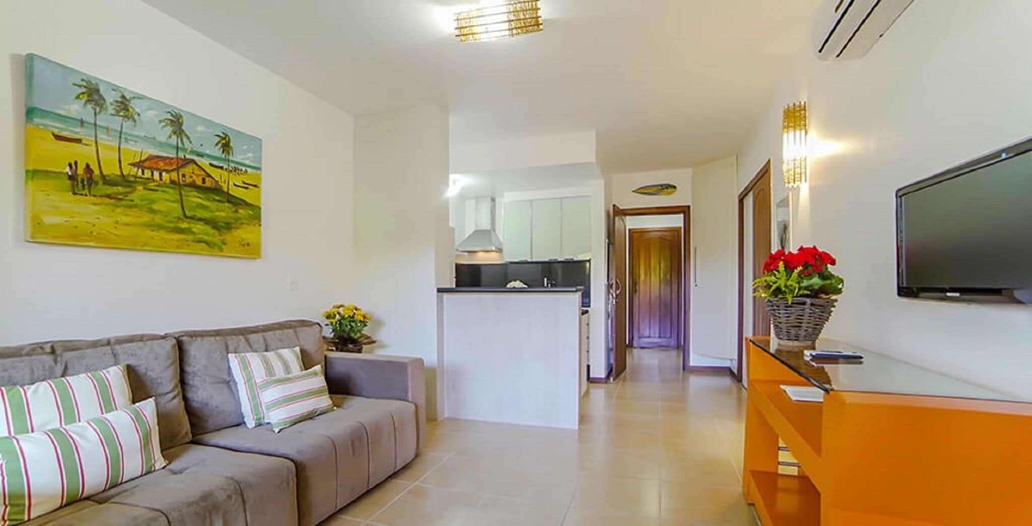A living room with a sofa, a painting, a TV, and a kitchen in the background.