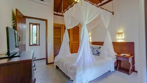 A bedroom with a canopy bed, a desk with a computer, and a bedside table with a lamp. - Mar Paraiso Hotel (Porto Seguro)