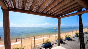 A wooden deck with potted plants, overlooking a beach with a clear view of the ocean. - Mar Paraiso Hotel (Porto Seguro)