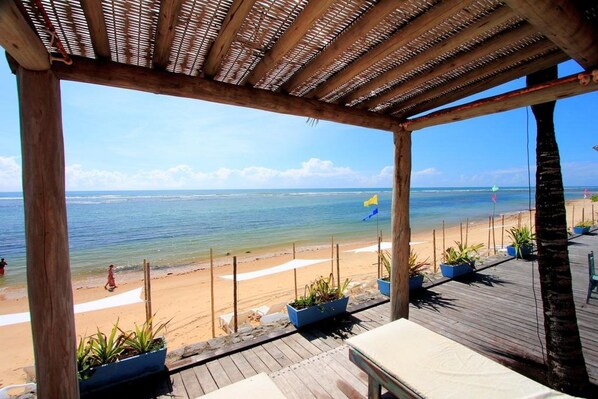 Una terraza de madera con plantas en macetas, con vista a una playa y una vista despejada del océano.