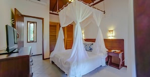 A bedroom with a canopy bed, a desk with a computer, and a bedside table with a lamp. - Mar Paraiso Hotel (Porto Seguro)