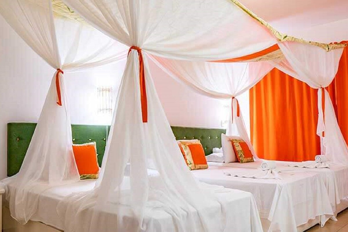 A hotel room with two beds, each covered with white sheets and a canopy.