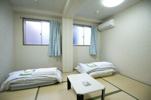 A small, clean room with two beds, a small table, and an air conditioning unit on the wall. - Hotel Mikado (Osaka)