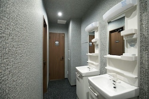 Un pasillo estrecho con dos lavamanos blancos y espejos, una puerta de madera y una pared con textura.