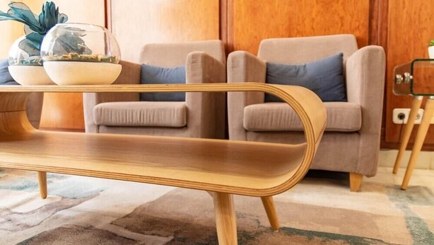 A modern living room with a wooden coffee table, two beige armchairs with blue cushions, and a glass-top side table with decorative items. - Hotel J. Balmes Vic (Vic)