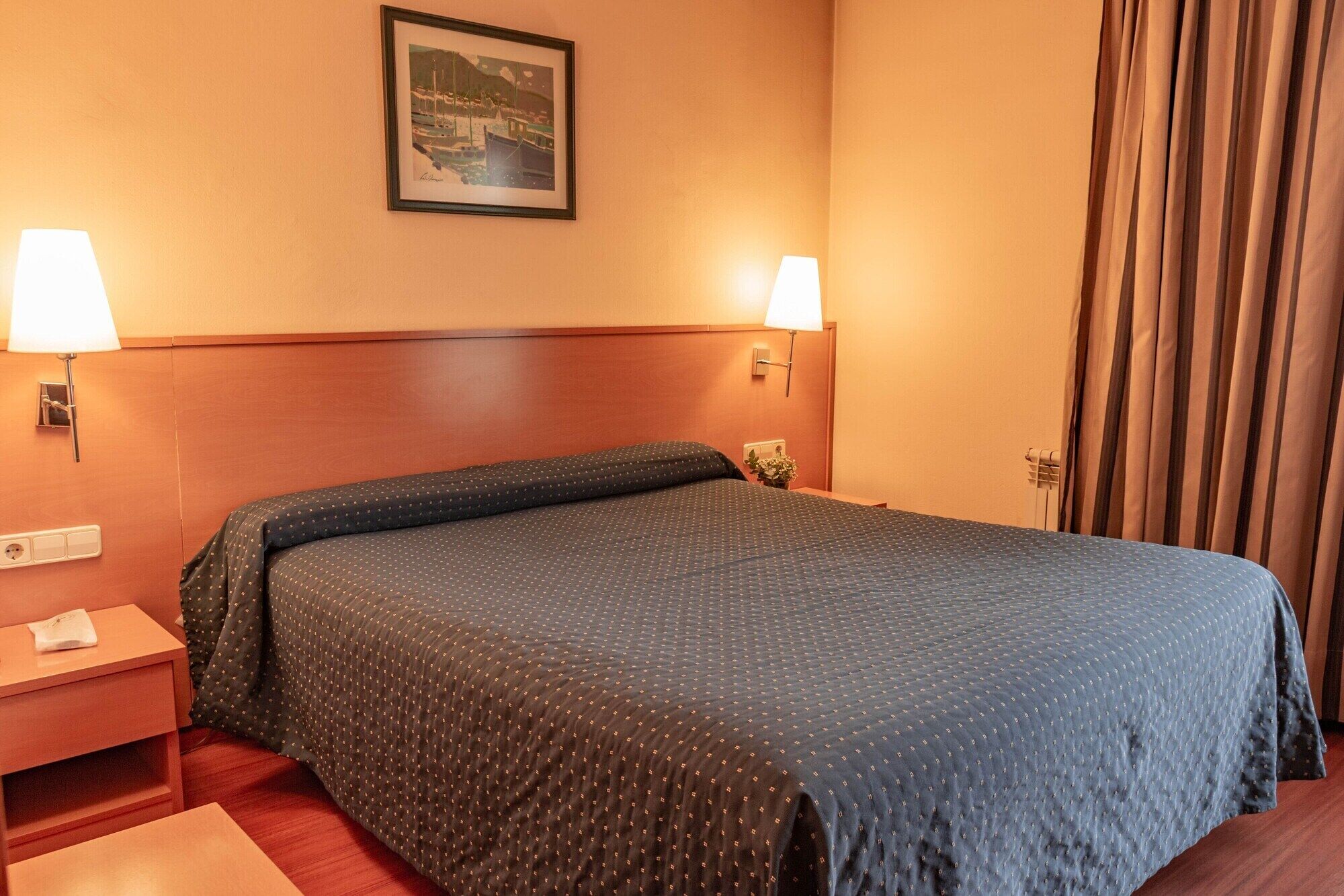 Habitación de hotel con cama, dos lámparas de noche, una mesita de noche, un cuadro en la pared y una ventana con cortinas.