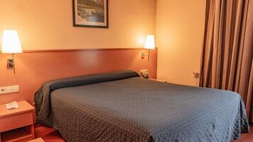 Habitación de hotel con cama, dos lámparas de noche, una mesita de noche, un cuadro en la pared y una ventana con cortinas.