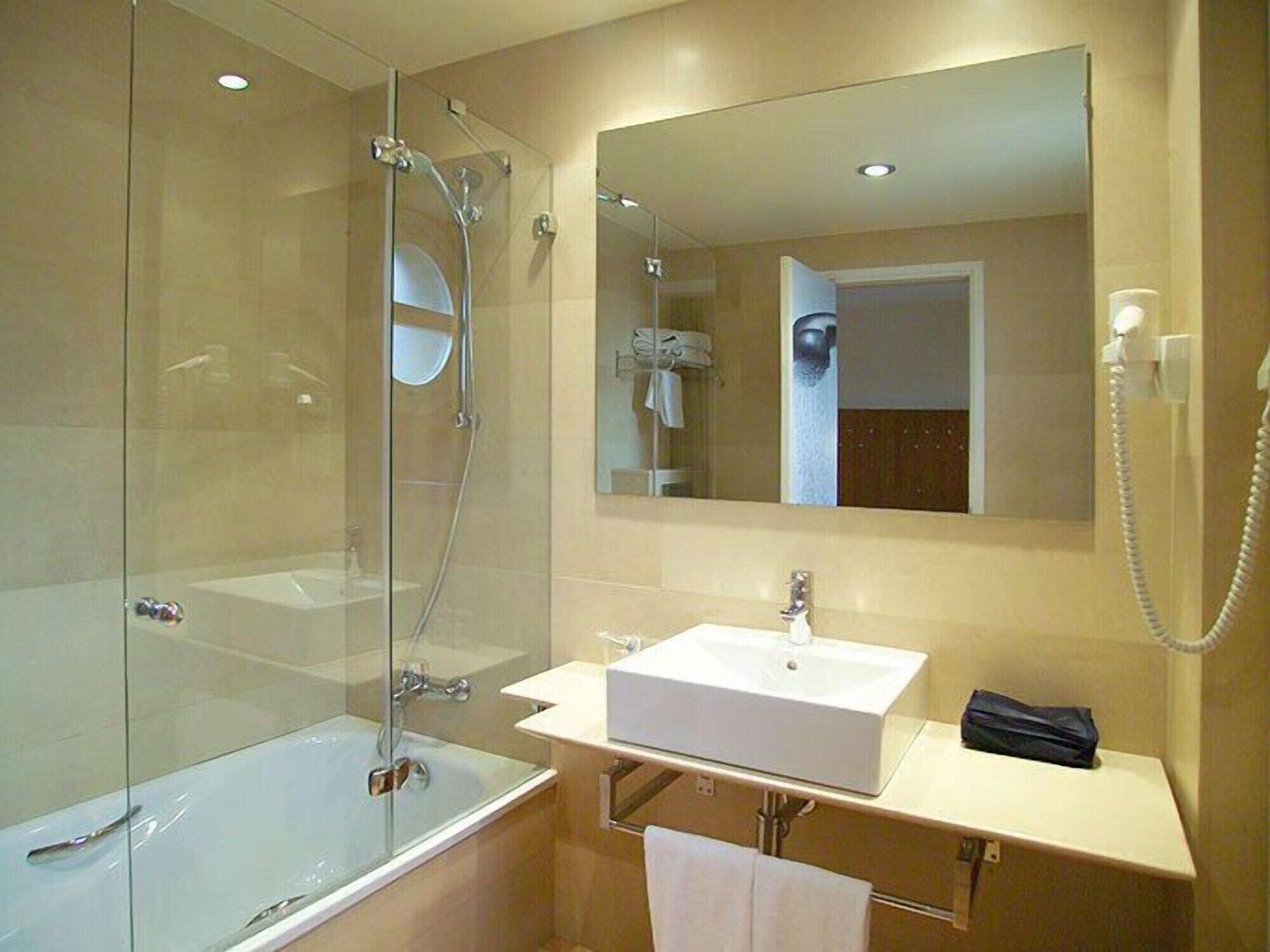 A modern bathroom with a glass-enclosed shower, a white sink, and a large mirror above the vanity.