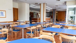 A dining area with multiple tables and chairs, a bar in the background, and a view of the outside through a large window. - Hotel J. Balmes Vic (Vic)