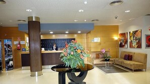 Een ontvangsthal met een balie, een grote pilaar, een moderne tafel met bloemdecoratie, een bank en kunstwerken aan de wanden.