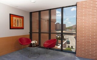 Una habitación con un ventanal grande, dos sillas rojas, una mesita y un cuadro en la pared.