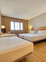 Una habitación de hotel con dos camas, un escritorio con lámpara y una ventana con cortinas.