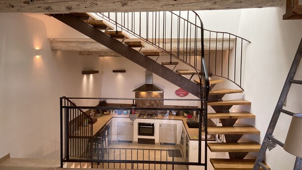 A modern kitchen with a central island, a built-in oven, and a stainless steel range hood. A spiral staircase with wooden steps and black metal railings leads to an upper level. - Gîte de Locre Citron en Luberon (Gargas)