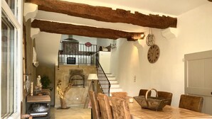 A rustic dining area with a wooden table, chairs, and a chandelier. A staircase leads to an upper level with a kitchen. - Gîte de Locre Citron en Luberon (Gargas)