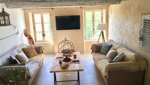 A cozy living room with two sofas, a coffee table, a TV, and a window with a view of greenery. - Gîte de Locre Citron en Luberon (Gargas)