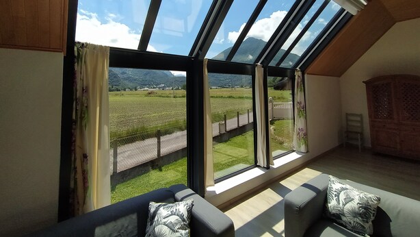 A room with a large skylight, a sofa with patterned cushions, and a view of a green landscape with a fence and a road. - House with breathtaking view of the mountains (Adast)