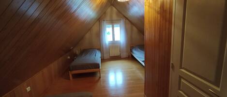 Un pequeño dormitorio en el ático con paredes de madera, techo inclinado y una sola ventana.