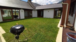 A backyard with a barbecue grill, a carport, and a house with large windows and a tiled roof. - House with breathtaking view of the mountains (Adast)
