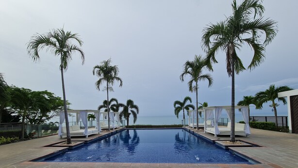 Una piscina con zonas de estar cubiertas por toldos blancos y palmeras.
