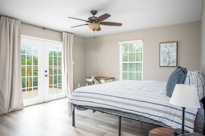 Ein Schlafzimmer mit einem Bett, einem Schreibtisch, einem Stuhl, einem Deckenventilator und einem Fenster mit Jalousien.