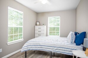 A bedroom with a bed, dresser, and two windows.