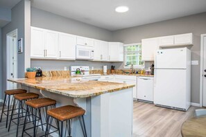 A modern kitchen with white cabinets, a granite countertop, and a built-in island with bar stools. - The River Rock Retreat (Bandera)