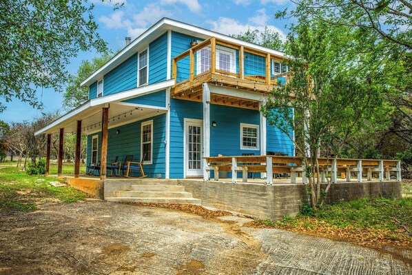 A two-story house with a porch, a covered outdoor seating area, and a concrete retaining wall.