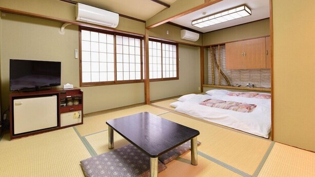 A traditional Japanese room with tatami flooring, a television, a small refrigerator, a wooden cabinet, and a bed with white bedding. - City Hotel Seiunso (Sakai)