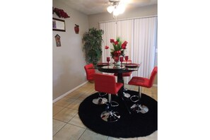 Cozy dining area with a round table and four chairs, set with a vase of flowers and wine glasses.