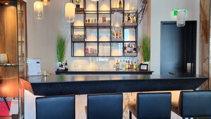 Uma área de bar com bancada de mármore, banquetes pretos e luminárias pendentes.