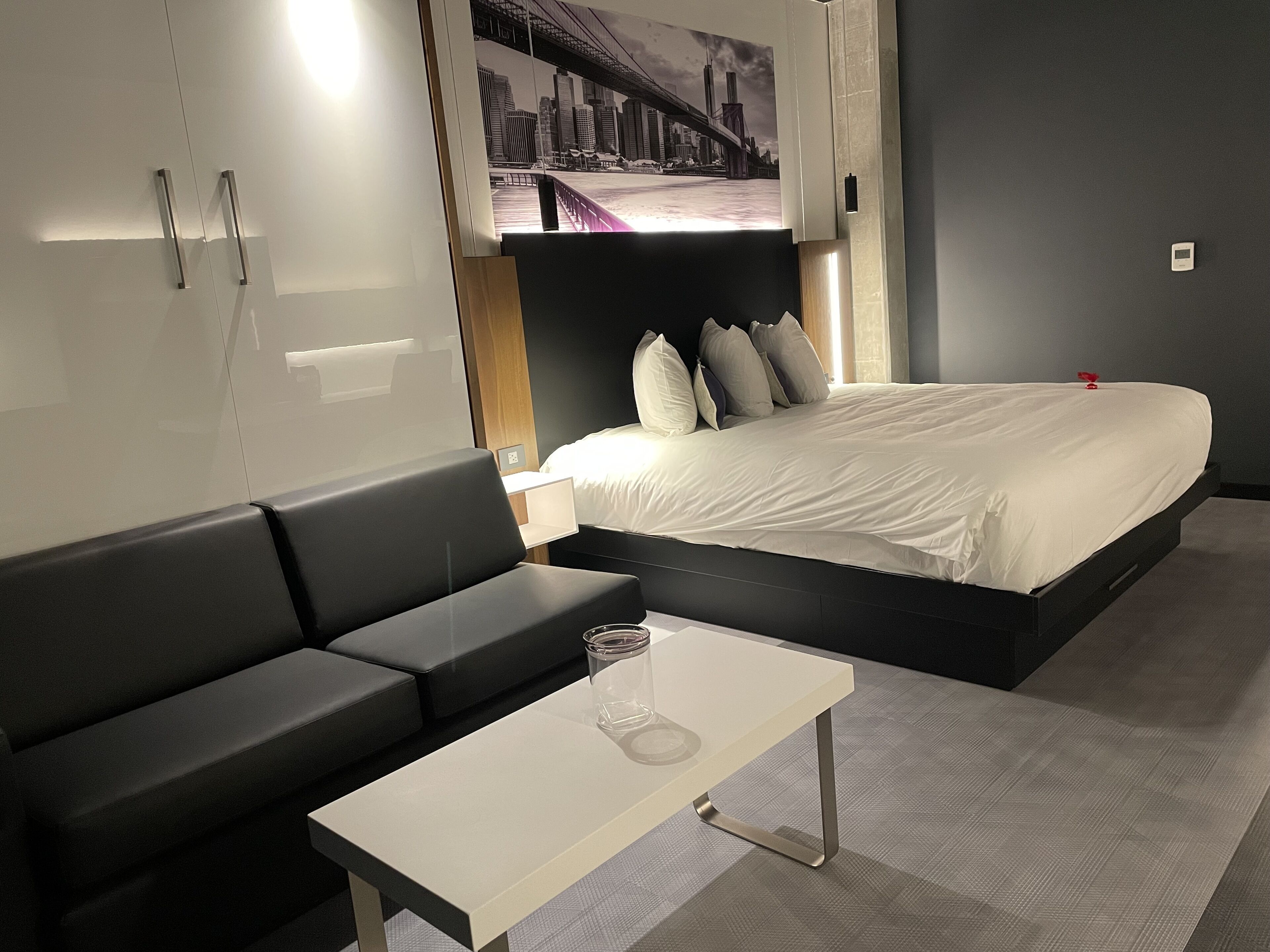 Una habitación de hotel moderna con una cama, un sofá, una mesita y un cartel con un paisaje urbano en la pared.