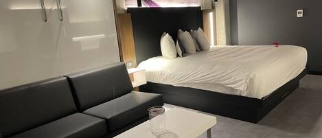 Una habitación de hotel moderna con una cama, un sofá, una mesita y un cartel con un paisaje urbano en la pared.
