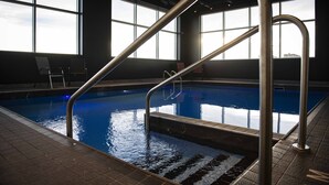 Uma piscina interior com paredes de vidro transparente, corrimãos de metal e chão revestido de azulejos.