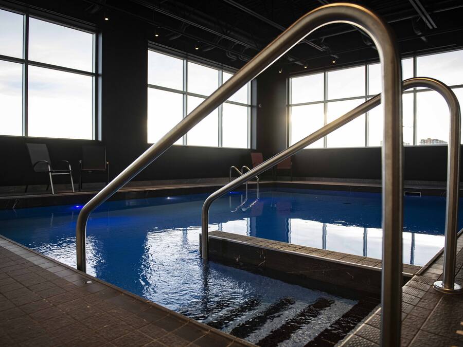 Una piscina interior amb parets de vidre transparent, baranes de metall i un paviment de rajoles.