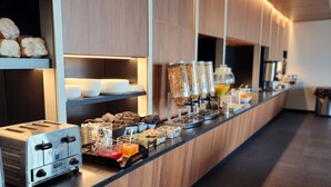 Buffet montado com torradeira, diversos recipientes de comida e máquina de café.